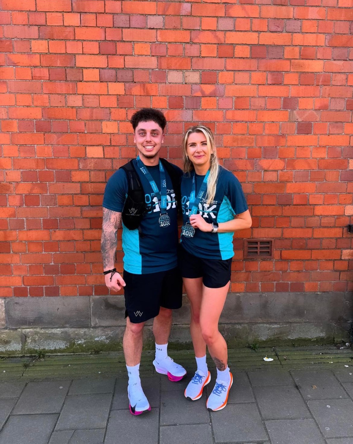 Two people standing against a brick wall wearing matching outfits.
